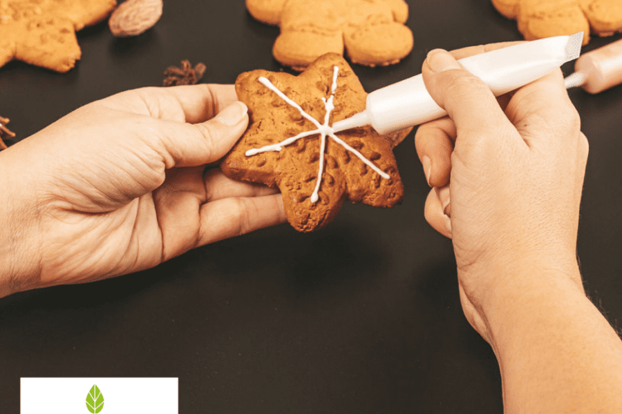 Hands piping icing on a star-shaped gingerbread biscuit, with Food Paper logo watermark, showcasing baking and decoration process.