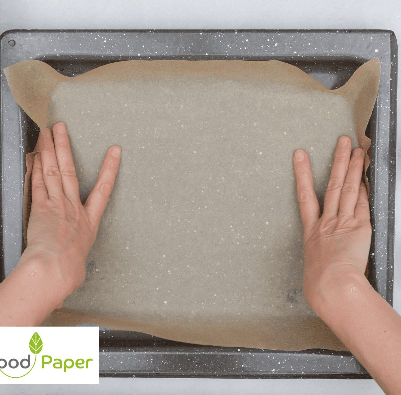 Hands placing parchment baking paper onto a tray, Food Paper logo watermark, highlighting non-stick baking preparation.