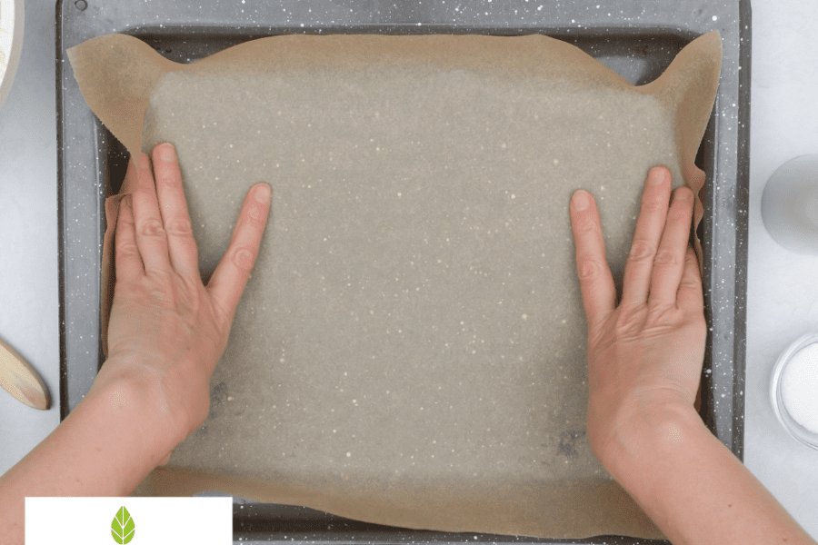 Hands placing parchment baking paper onto a tray, Food Paper logo watermark, highlighting non-stick baking preparation.