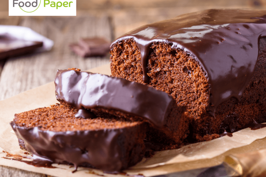 Freshly sliced chocolate loaf cake topped with glossy icing, served on Food Paper parchment with brand logo watermark.