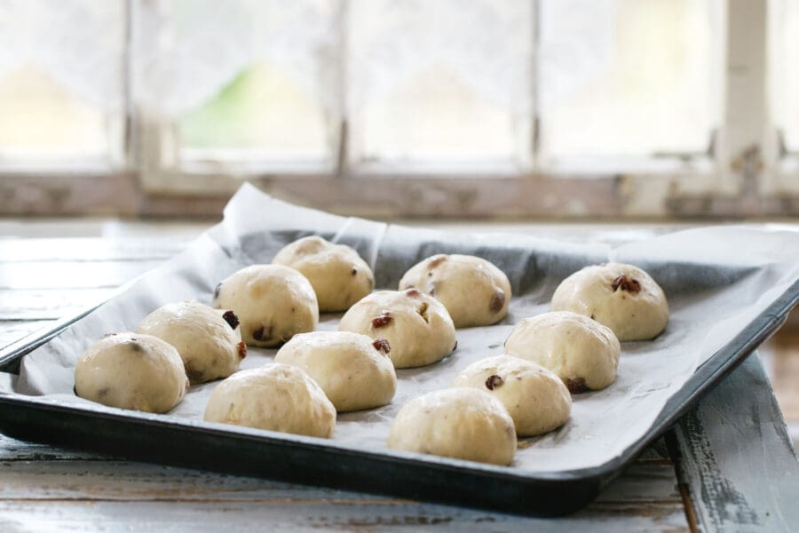 Fresh dough balls with raisins resting on a tray lined with non-stick silicone baking paper in a rustic kitchen setting.