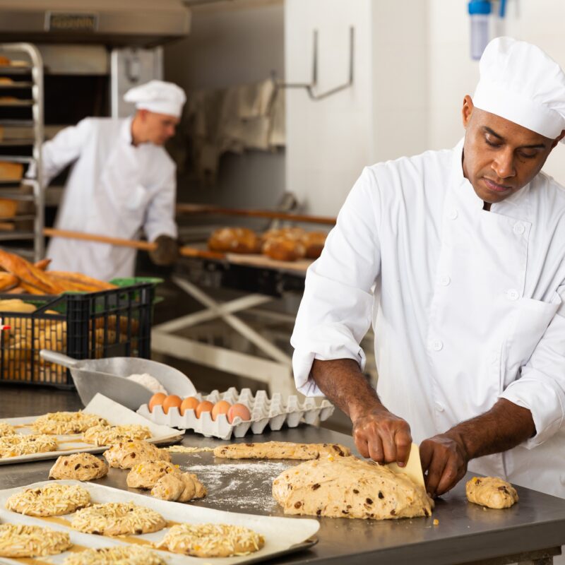 Professional bakers in a commercial bakery preparing dough and bread loaves, showcasing craftsmanship and food production.