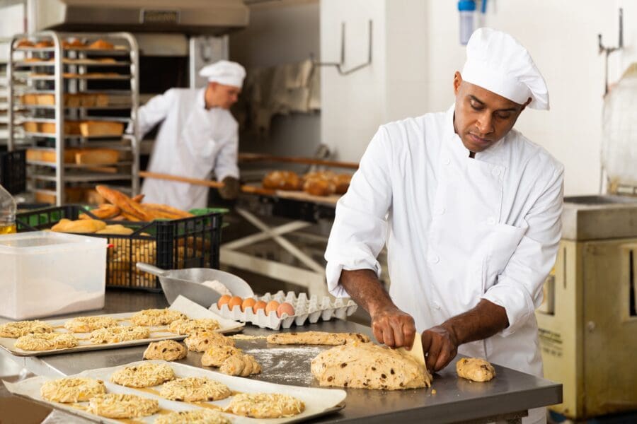 Professional bakers in a commercial bakery preparing dough and bread loaves, showcasing craftsmanship and food production.