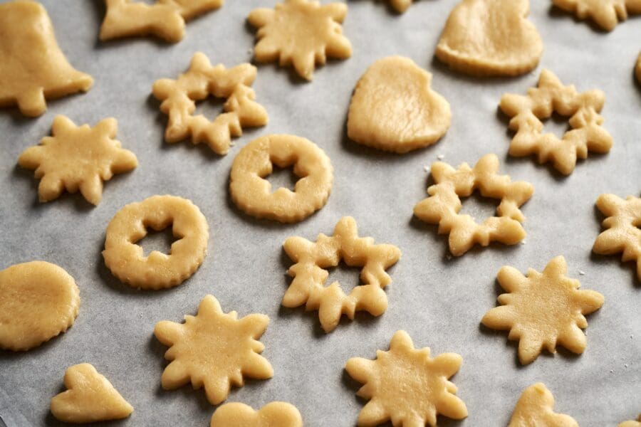 Assorted cookie dough shapes cut out and placed on baking paper, ready for baking festive treats.