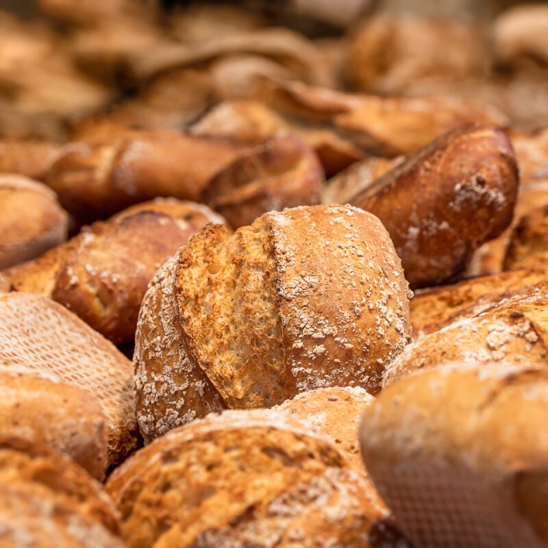 Golden rustic bread rolls with a crisp crust and flour dusting, freshly baked and displayed in a UK bakery.
