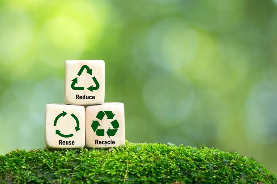 Wooden blocks showing reduce, reuse, recycle symbols on moss with a blurred green background, promoting sustainability practices.