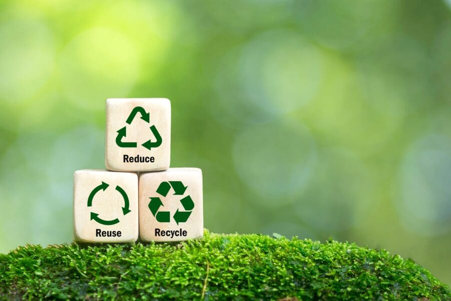 Wooden blocks showing reduce, reuse, recycle symbols on moss with a blurred green background, promoting sustainability practices.