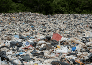 Large landfill site overflowing with plastic waste, bags, and mixed rubbish piled high.