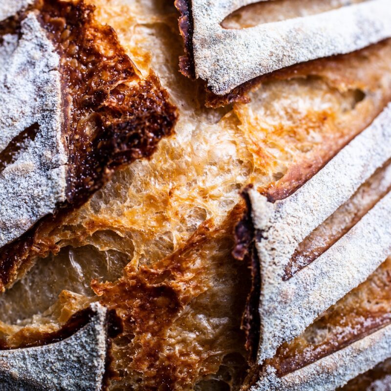 Detailed close-up of golden artisan bread crust with flour-dusted scoring, showing texture, crispness, and baking quality.
