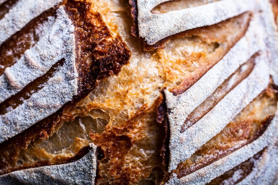 Detailed close-up of golden artisan bread crust with flour-dusted scoring, showing texture, crispness, and baking quality.
